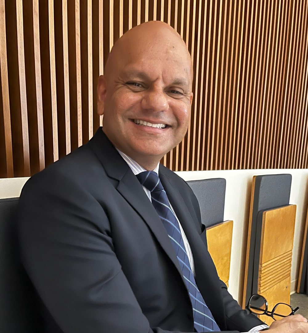 Dr. Peter Maharaj smiling, seated in a dark suit